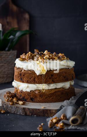 Layered carrot cake topped with thick cream cheese frosting, caramelised walnuts and a drizzle of honey on a rustic board. Stock Photo
