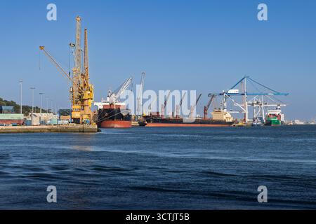 Commercial port of Setúbal, Portugal, featuring cargo ships, large cranes, and heavy industrial equipment against a clear blue sky. Setubal, Portugal. Stock Photo