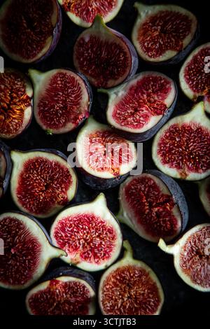 Halved ripe figs displaying ruby red interiors arranged tightly on a dark moody background for dramatic produce imagery. Stock Photo