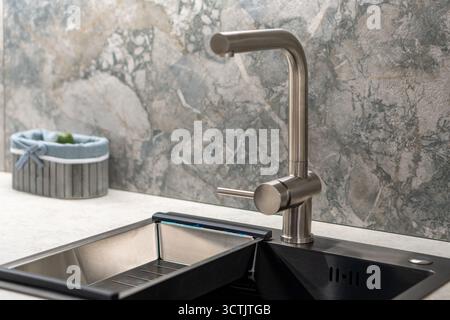 A stainless steel kitchen faucet on an artificial stone sink in a marble-style kitchen. Stock Photo