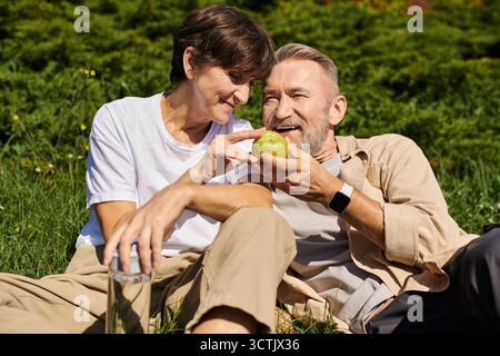 Senior couple shares a delightful time outdoors, laughing and connecting over a fresh apple. Stock Photo