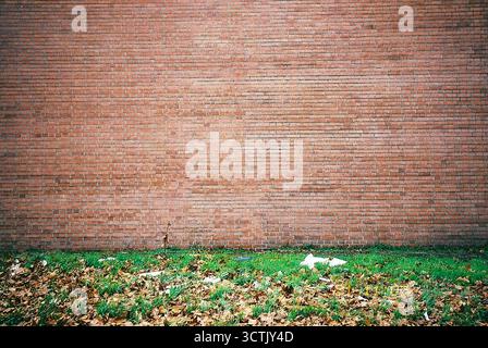 Large empty red brick wall with a side wall and a patch of grass at the bottom, captured in analog snapshot style. Stock Photo
