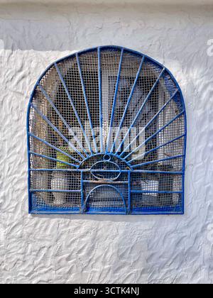 Decorative sunburst grille over arched window on white textured wall, Martil, Tetouan, Morocco, 6 October 2025. Stock Photo