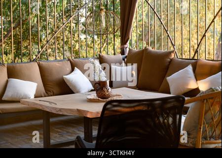 Corner sofa with brown pillows and wooden table on outdoor terrace with decor Stock Photo