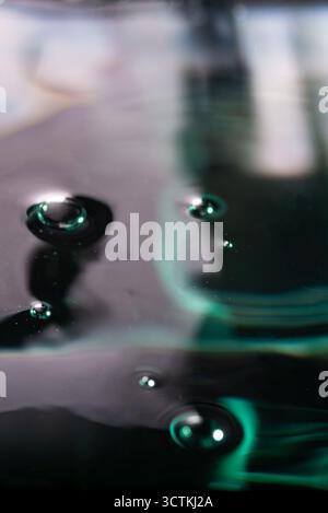 277.Small bubbles scatter across glossy dark liquid with green-blue reflections. Lighting and texture highlight fluid motion, surface tension, and abs Stock Photo