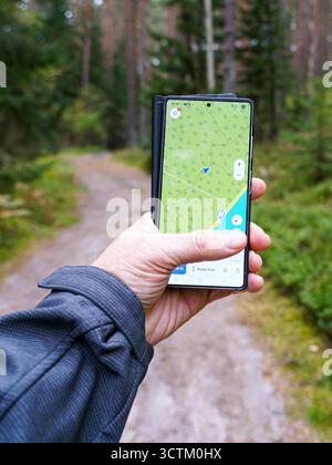 Close-up of a hand using a smartphone with GPS map app while walking on a forest trail, symbolizing navigation, hiking, and outdoor adventure Stock Photo