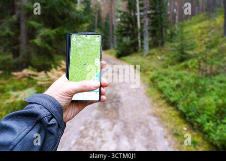 Close-up of a hand holding a smartphone with GPS map app open on a forest trail, symbolizing hiking, navigation, exploration, and outdoor orientation Stock Photo