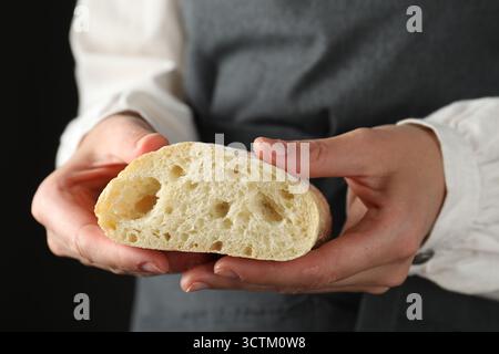 Woman holding half of fresh ciabatta on black background, closeup Stock Photo