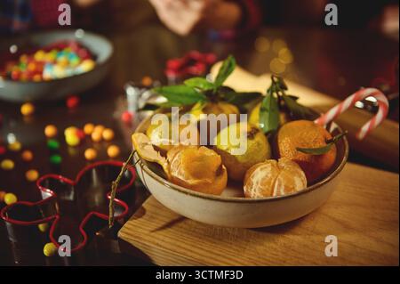 A rustic bowl filled with peeled oranges and other citrus sits on a wooden board beside candy canes, evoking a festive, cozy kitchen scene. Stock Photo