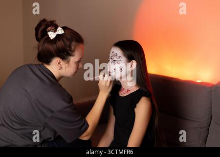 Woman painting girl's face with intricate designs, both smiling Stock Photo
