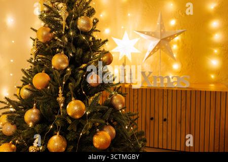 Golden baubles on a Christmas tree with warm fairy lights and bokeh, a cozy festive interior background ideal for seasonal ads, cards, and social medi Stock Photo