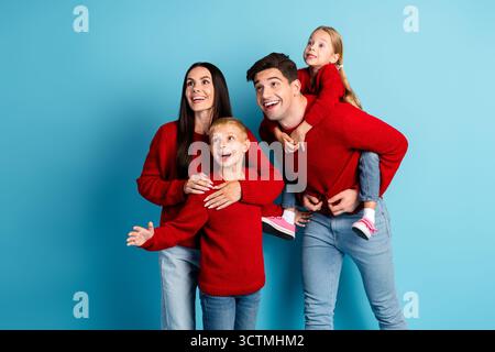 Happy family of four in red sweaters enjoying winter holiday moments together against a bright blue background Stock Photo