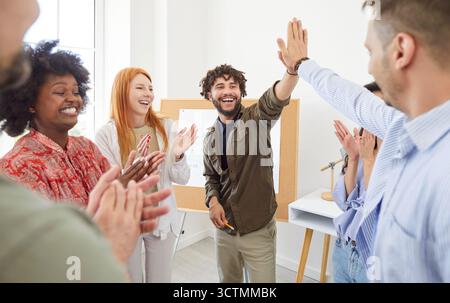 Multiracial team of young people celebrating success after meeting or training, giving high five. Stock Photo