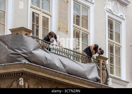 Two workers covering a balcony with protective material, engaged in maintenance work on a historic building in Prague, Czech Republic on 3 July 2024 Stock Photo