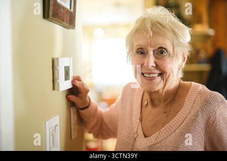 senior lady posing at home portrait close to a window using thermostat Stock Photo