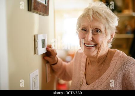 senior lady posing at home portrait close to a window using thermostat Stock Photo