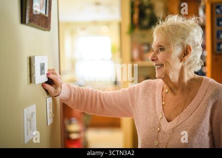 senior lady posing at home portrait close to a window using thermostat Stock Photo
