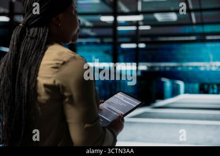 Data center admin uses tablet to monitor hardware for potential failures, improving system stability. Server hub IT professional configures supercomputers settings with device to increase uptime Stock Photo