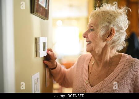 senior lady posing at home portrait close to a window using thermostat Stock Photo