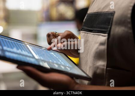 Close up of female warehouse employee checking cargo dispatch details next to storage racks, solving shipment logistics to ensure seamless import export operations. Online shopping large business. Stock Photo