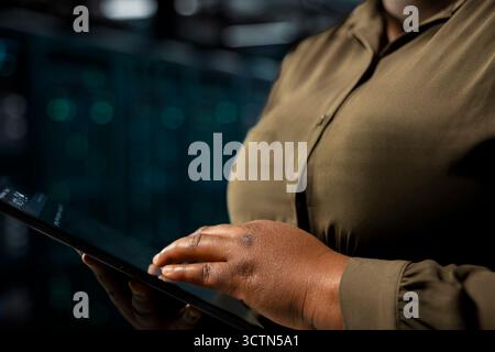 Close up of data center engineer using tablet to optimize network infrastructure, planning capacity. IT specialist managing server farm resources with device for improved reliability and uptime Stock Photo