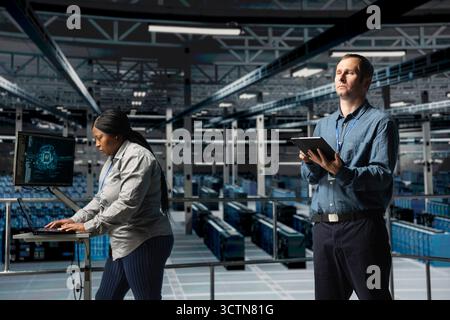 Server farm team of technicians using devices to do infrastructure AI machine learning automatization. Data center programmer and coworker doing maintenance using artificial intelligence Stock Photo