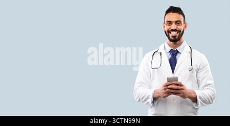 Arab Doctor Man Holding Smartphone Using Medical Application, Blue Background Stock Photo