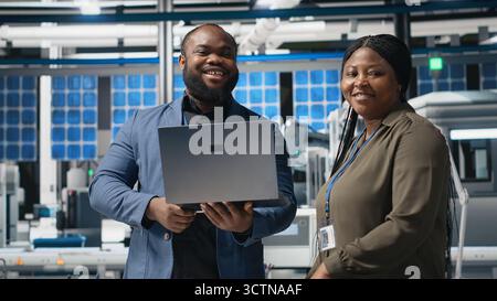 Black factory inspectors engaging in a briefing over the manufacturing process, reviewing production line and metrics on files. Supporting renewable energy improvement. Camera B. Stock Photo