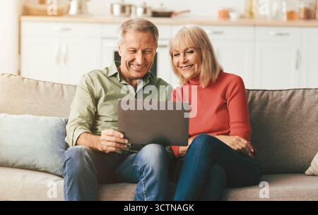 Cheerful Senior Spouses Using Laptop Watching Movie Onilne At Home Stock Photo