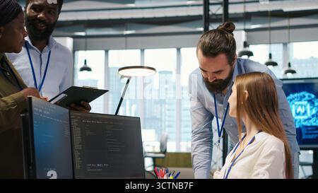 Welcoming team assisting intern developing artificial intelligence models for business analytics. Friendly coworkers helping junior dev running simulations for AI driven forecasting, camera A Stock Photo