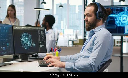 Software developer coding with AI language model assistance in office, listening music. Programmer wearing headphones integrating LLM assistant suggestions into code editor, camera A Stock Photo