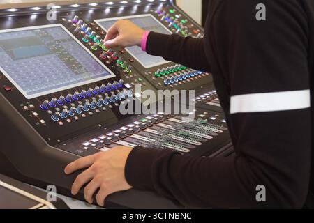 Sound engineer's hand on a professional audio mixing console. Technician adjusting fader in a broadcast control room. Stock Photo