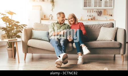 Cheerful Mature Spouses Using Digital Tablet At Home Stock Photo