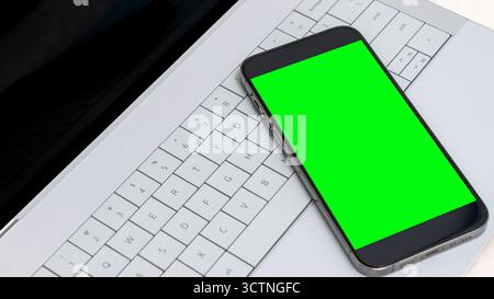 Smartphone mock up featuring a vibrant green screen, positioned on a stylish laptop keyboard, ideal for showcasing digital design concepts and creativ Stock Photo