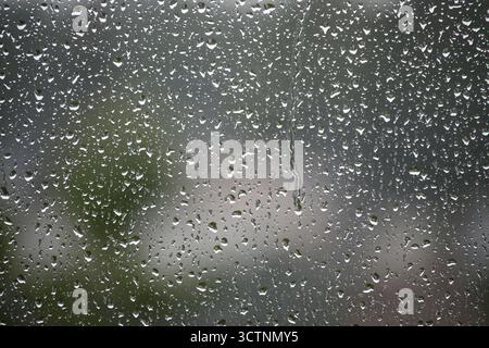 Close-up of raindrops on a window, creating a mesmerizing pattern. Blurred background with hints of nature. Stock Photo