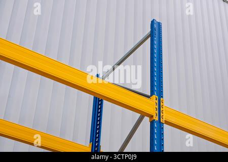 Industrial warehouse racking system with yellow beams and blue uprights. Close-up view of corrugated white wall background. Heavy-duty shelving used i Stock Photo