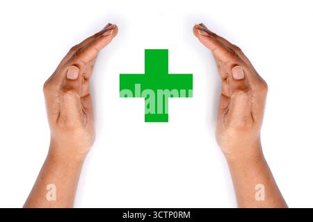Green medical cross covered by hands on white background. Stock Photo