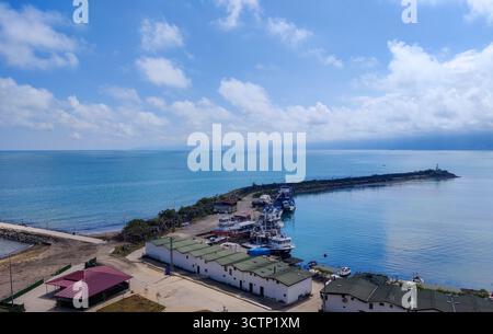 Aerial view of coastal harbor with docked fishing boats. The scene captures a calm coastal morning with cloudy skies and gentle waves reflecting soft Stock Photo