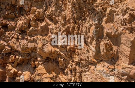 Close-up of rugged rocky cliff surface. Detailed view of a rugged rock face showcasing its jagged. Weathered texture and earthy tones. Backgrounds or Stock Photo