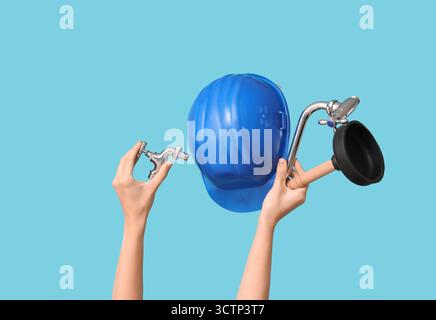 Hands with hardhat and plumber supplies on blue background Stock Photo