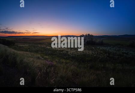 Wide angle panoramic shot capturing the serene transition from day to night over a vast rural landscape. Fields and distant mountains silhouetted agai Stock Photo