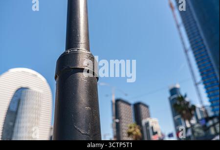 A minimalist city scene captured with a strong foreground focus on a black metal pole against blurred modern skyscrapers and a clear blue sky. Perfect Stock Photo