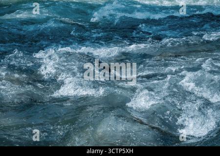 Dynamic shot capturing frothing movement of blue-tinged river water as it rushes over unseen obstacles. Untamed natural energy and motion. Stock Photo