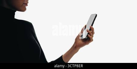 A silhouette of a person holding a smartphone against a plain white background highlights modern technology. Stock Photo