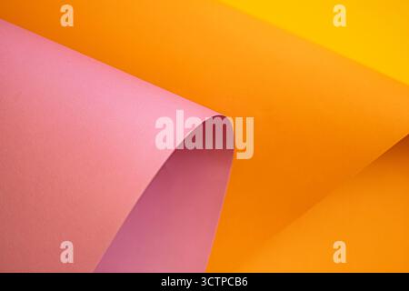 Abstract close-up of colorful sheets of paper in pink and yellow. The curved fold creates a smooth flowing shape. Highlighting vibrant tones and textu Stock Photo