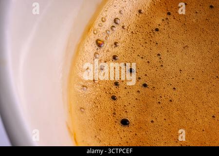 Close-up macro shot of freshly brewed coffee with rich foam and bubbles on the surface inside a white cup. Creamy coffee macro shot. Freshly brewed cu Stock Photo