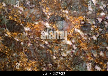 Close-up of natural granite stone surface showing multicolored mineral patterns. The detailed texture with green, gold and white tones highlights the Stock Photo