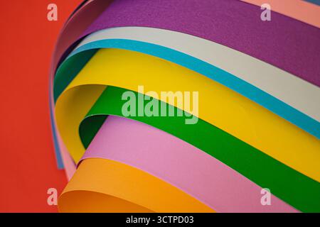 Colorful paper sheets arranged in a curved, layered pattern against a vibrant red background. Showcasing a spectrum of hues. Selective focus. Stock Photo