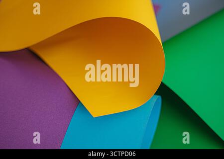 Curled yellow sheet over colorful papers. Yellow sheet curled over layers of purple, cyan and green paper. The image emphasizes smooth arcs. Stock Photo
