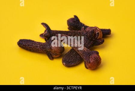 Close-up of dried cloves on a bright yellow background. Aromatic spice used in cooking, baking and traditional remedies. Strong scent and rich flavor. Stock Photo